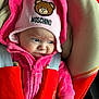 baby, child, pink, hat, hoodie, car_seat, seat_belt, red, clothing, face, person, infant, cute, expression, indoor, soft_fabric, moschino, furrowed_brow, portrait, snug