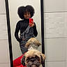 mirror, selfie, dog, red_sweater, person, afro_hair, black_turtleneck, overalls, smartphone, indoor, white_wall, tile_wall, reflection, standing, cute, pet, fur, small_dog, portrait, casual