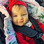 baby, child, car_seat, red_sweater, headband, red_bow, blanket, floral_pattern, infant, cute, smiling, indoors, seatbelt, safety_harness, portrait, face, skin, hand, cozy, comfort