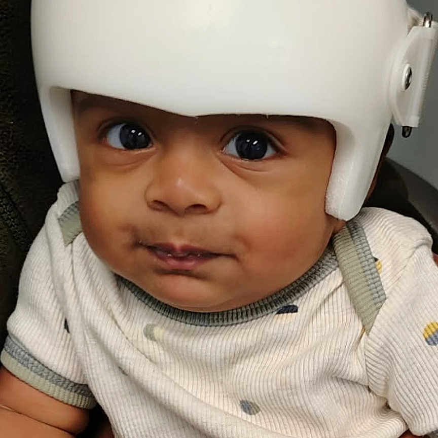Anvay is registered to the contest to win money with this photo: apparel, baby, child, clothing, cute, expression, eyes, face, hand, headgear, helmet, indoor, infant, person, portrait, protective_gear, sitting, skin, support, young