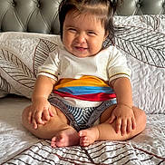 Zoe is registered to the contest to win money with this photo: baby, child, smiling, pigtails, sitting, bed, bedspread, pattern, clothing, bracelet, indoors, happy, cute, portrait, person, skin, hair, foot, hand, furniture