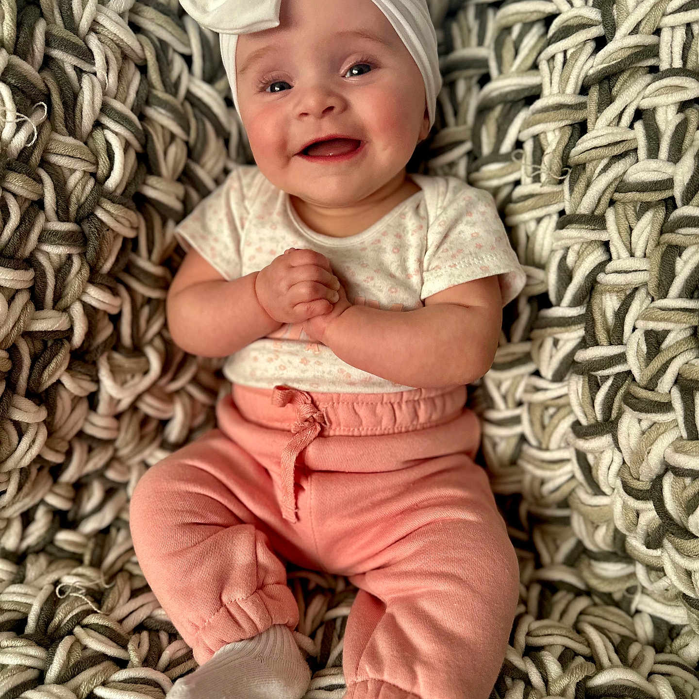 Jordee joined the competition — help win amazing prizes! baby, bow, child, clothing, cozy, cute, face, hands_clasped, happy, headband, indoors, infant, knit_blanket, person, pink_pants, portrait, sitting, smiling, soft_lighting, white_socks