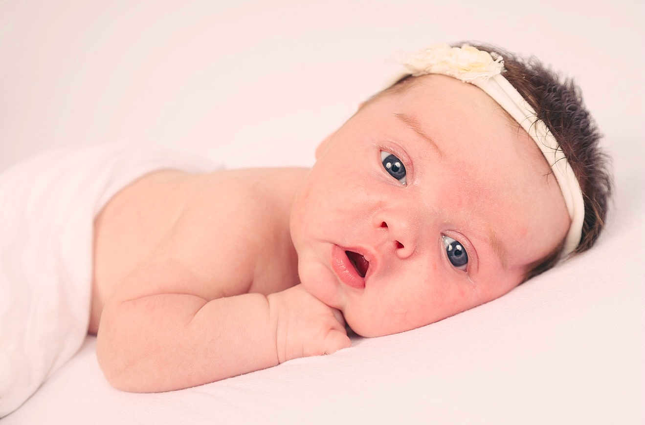 Issabella Rose is registered to the contest to win money with this photo: baby, infant, face, headband, flower, skin, arm, lying_down, cute, portrait, newborn, child, soft_light, expression, closeup, human, resting, peaceful, pink, white_background