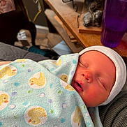 Luca joined the competition — help win amazing prizes! newborn, baby, sleeping, blanket, duck_pattern, beanie, indoor, cozy, soft, face, child, infant, wrapped, cute, peaceful, resting, warm_lighting, purple_cup, table, person