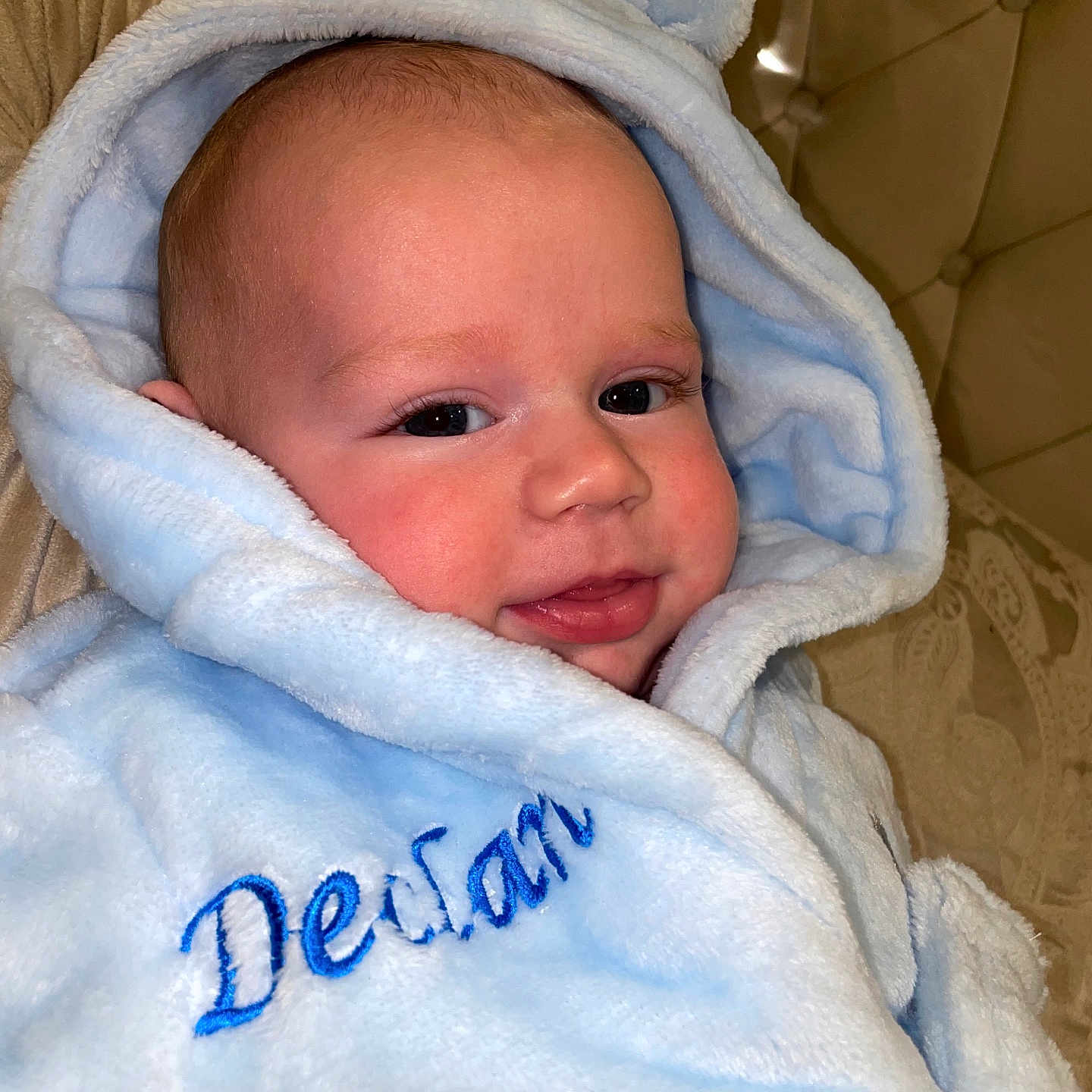 Declan is registered to the contest to win money with this photo: apparel, baby, blanket, blue, child, comfort, cozy, cute, expression, face, fur, hood, indoors, infant, person, portrait, sleepwear, smile, soft, warm