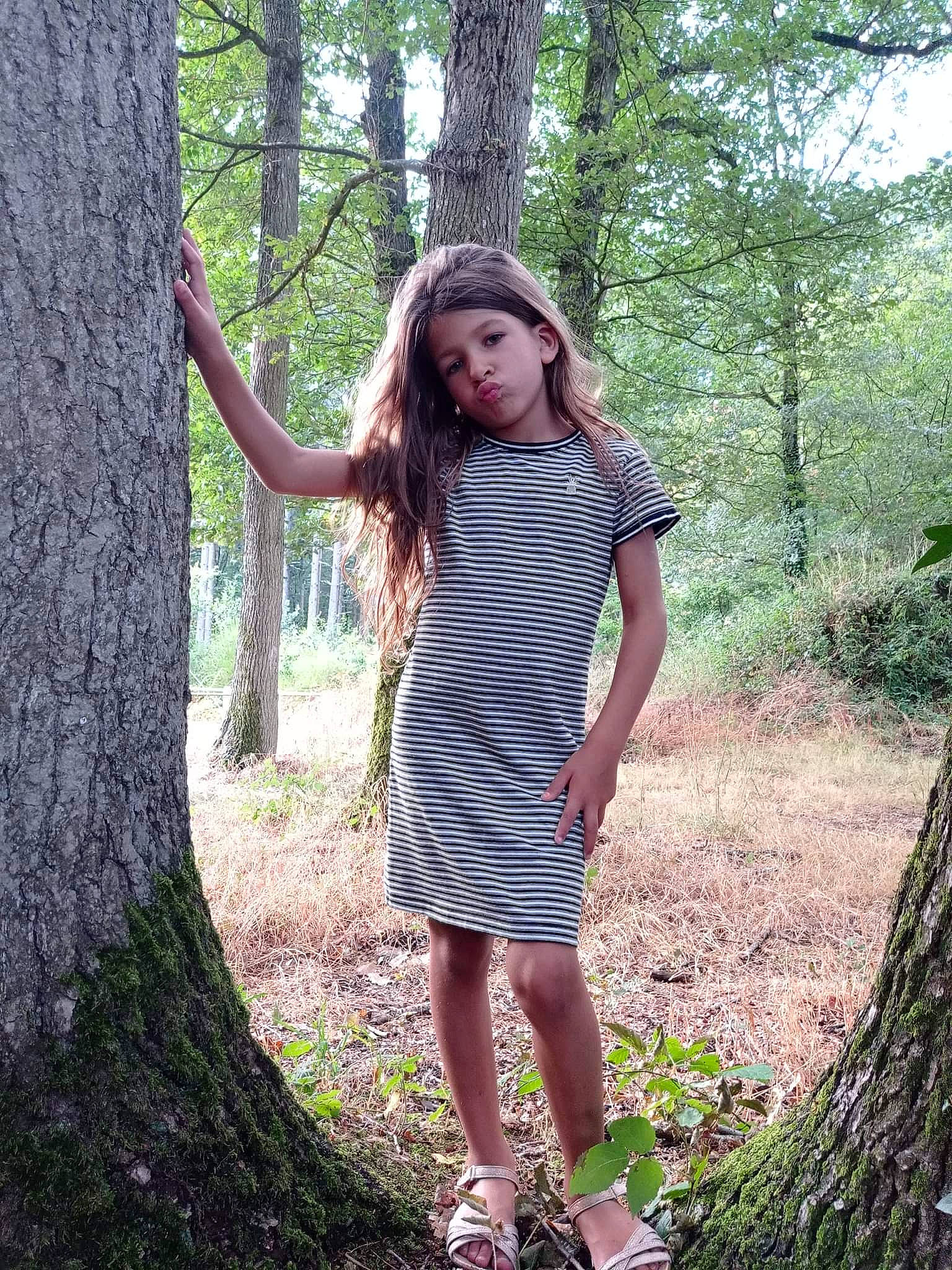 Lyna participe au concours pour gagner de l'argent avec cette photo : brown_hair, day_dress, fawn, flash_photography, forest, grass, human_leg, knee, long_hair, pattern, people_in_nature, person, plant, street_fashion, sunlight, thigh, tree, trunk, waist, wood