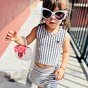Leah is registered to the contest to win money with this photo: child, toddler, sunglasses, striped_clothing, top, skirt, shoes, sneakers, handbag, bracelet, sunny, outdoor, sidewalk, railing, posing, fashion, cute, person, portrait, young