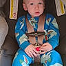 Dominic is registered to the contest to win money with this photo: toddler, child, car_seat, blue_pajamas, dinosaur_pattern, seatbelt, baby, indoor, warning_label, clothing, person, infant, sitting, cute, young_child, face, expression, hands, safety, plush