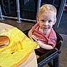 Dominic is registered to the contest to win money with this photo: toddler, child, high_chair, fast_food, cheeseburger, french_fries, ketchup, table, restaurant, indoor, blonde_hair, blue_eyes, striped_shirt, curious, seated, food, meal, plastic_chair, floor, metal_bars