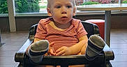 Dominic joined the competition — help win amazing prizes! toddler, child, high_chair, red_onesie, socks, indoor, window, greenery, table, chair, floor_tiles, casual, daylight, curious, seated, person, baby, expression, legs_up, restaurant