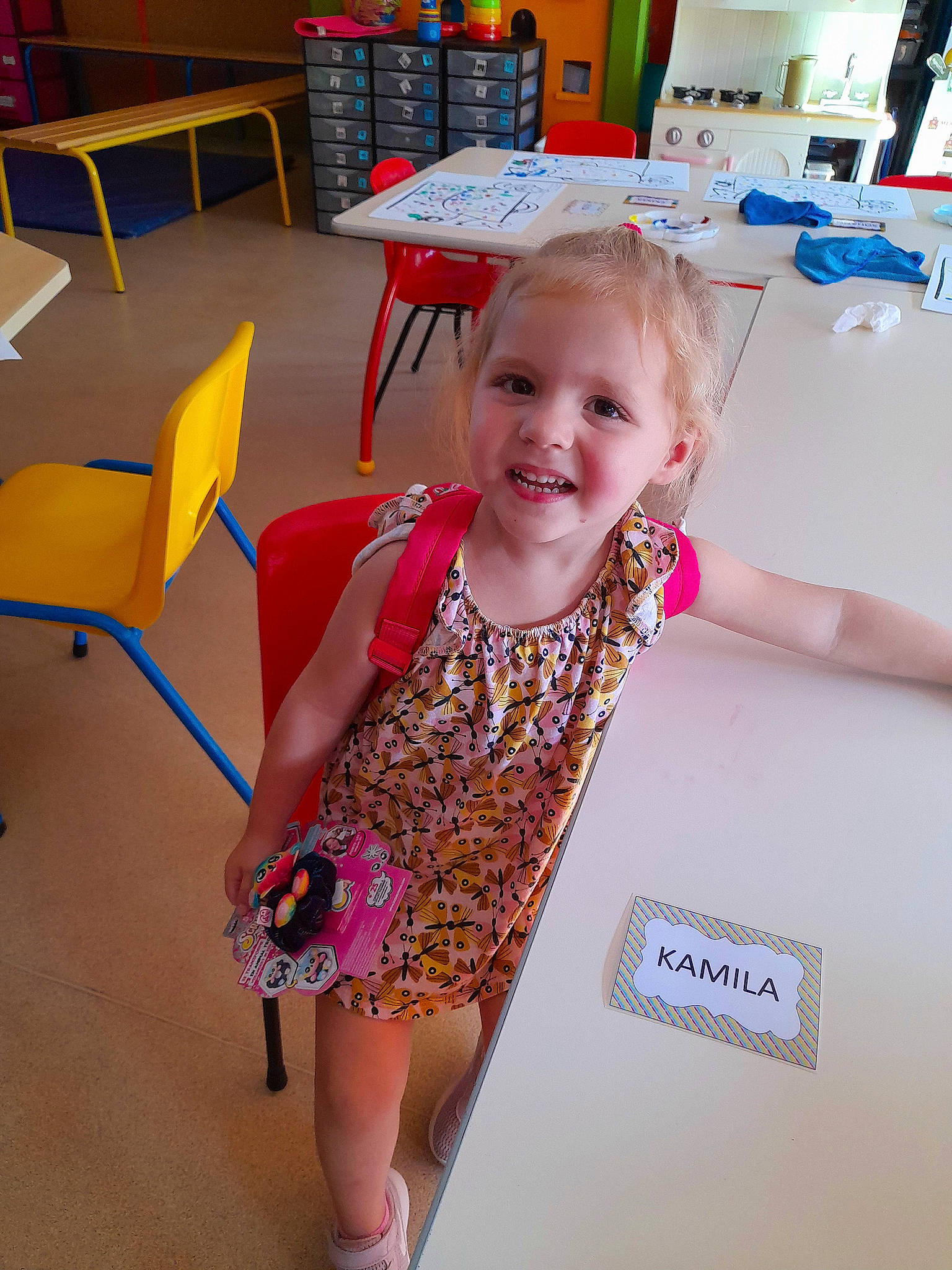 Kamila participe au concours pour gagner de l'argent avec cette photo : bookcase, chair, child, flooring, fun, happy, human_leg, joy, leisure, magenta, pattern, person, room, sandal, shelf, shelving, sitting, smile, summer, t_shirt
