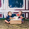 child, toddler, cake, watermelon, food, messy, indoor, floor, playful, smiling, sitting, frosting, hands, face, blue_clothing, dress, basket, background, vintage_wall, happy