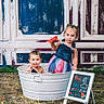 Reigna is registered to the contest to win money with this photo: child, toddler, watermelon, metal_tub, chalkboard, grass, playful, summer, outdoor, dress, smiling, tongue_out, stars, patriotic, background, fun, cute, two_children, advertisement, food