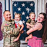 Reigna is registered to the contest to win money with this photo: family, soldier, military_uniform, toddler, child, woman, smiling, happy, embrace, portrait, american_flag, background, tattoo, holding, indoor, people, casual, joyful, cute, togetherness
