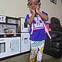 child, girl, indoor, colorful_clothing, backpack, toy_kitchen, carpet, leather_chair, smiling, standing, hair_beads, first_grade, playroom, shoes, leggings, purple_shirt, home, furniture, portrait, cute