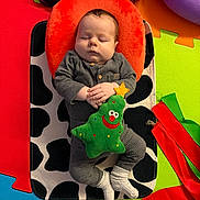 Caleb is registered to the contest to win money with this photo: baby, sleeping, plush_toy, christmas_tree, gray_clothing, orange_pillow, black_and_white_mat, colorful_play_mat, foam_mat, ribbons, infant, cozy, child, indoors, floor, hands_folded, sock, toy, peaceful, soft_texture