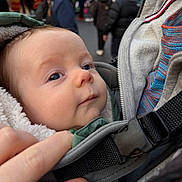Caleb is registered to the contest to win money with this photo: baby, baby_carrier, blurred_background, child, closeup, coat, crowd, face, green_nails, hand, infant, jacket, nail_polish, outdoor, people, person, portrait, street, urban, winter_clothing