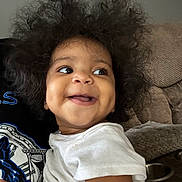 Dyllan joined the competition — help win amazing prizes! toddler, child, smile, happy, curly_hair, white_shirt, indoor, person, face, couch, furniture, skin, portrait, cute, baby, young_child, joy, expression, sitting, human
