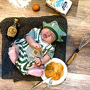 Loann a rejoint le concours — aidez-le/la à gagner de superbes lots ! baby, infant, chef_hat, striped_clothing, pancakes, fork, knife, whisk, egg, maple_syrup, flour, plate, wooden_floor, cooking, food, nap, cute, sleeping, kitchen, recipe
