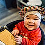 baby, child, smiling, hat, red_clothing, high_chair, table, wooden_table, indoor, happy, face, cute, person, infant, warm_clothing, striped_hat, cheerful, hands, sitting, portrait