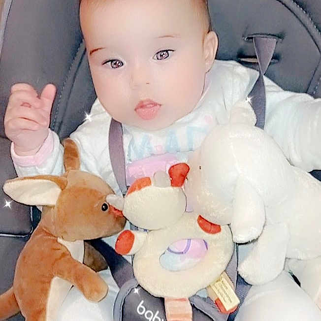 Iona a rejoint le concours — aidez-le/la à gagner de superbes lots ! baby, baby_carrier, child, child_seat, comfort, cute, face, hands, happy, head, indoor, infant, legs, pink_socks, plush_toy, seat_belt, smiling, soft_toy, stuffed_animal, white_clothing