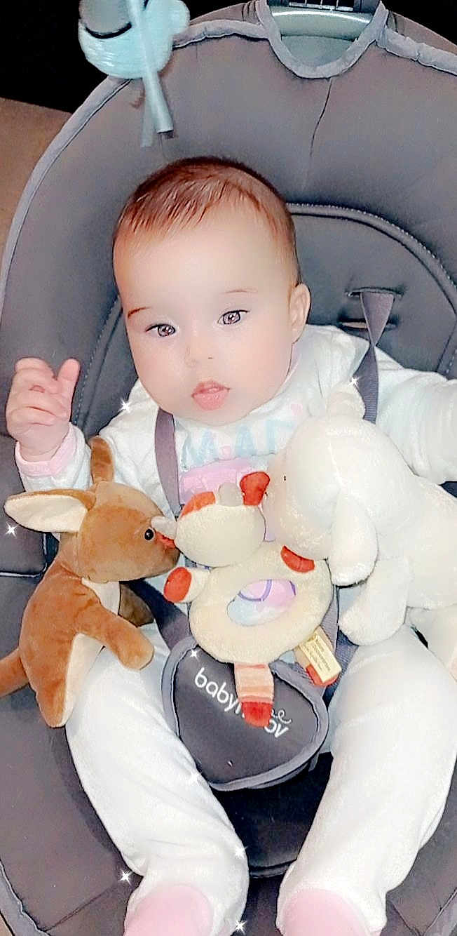 Iona a rejoint le concours — aidez-le/la à gagner de superbes lots ! baby, infant, plush_toy, stuffed_animal, baby_carrier, white_clothing, pink_socks, cute, child, seat_belt, soft_toy, indoor, smiling, face, head, hands, legs, comfort, happy, child_seat