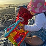 María Jose Sua Baron is registered to the contest to win money with this photo: toddler, child, toy, beach, sunset, hat, strawberry_pattern, denim_overalls, blanket, sand, outdoor, playtime, colorful_toy, summer, sunlight, side_view, sitting, family_time, relaxation, nature