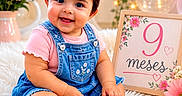 María Jose Sua Baron joined the competition — help win amazing prizes! baby, girl, smiling, denim_dress, pink_shirt, white_shoes, flowers, pink_bow, fairy_lights, fluffy_rug, sign, milestone, portrait, cute, indoor, celebration, sitting, happy, headband, decor