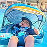 baby, blue, canopy, child, float, happy, hat, infant, outdoor, playful, relaxing, safety_harness, smile, summer, sunlight, swimming_pool, swimwear, thumbs_up, vacation, water