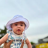 Dezi joined the competition — help win amazing prizes! baby, child, hat, white_hat, dinosaur_print, outdoor, tattoo, person, infant, cute, portrait, holding_hands, clothing, sky, daylight, face, expression, young_child, summer, casual