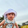 baby, child, hat, white_hat, dinosaur_print, outdoor, tattoo, person, infant, cute, portrait, holding_hands, clothing, sky, daylight, face, expression, young_child, summer, casual