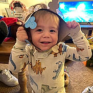 Benjamin joined the competition — help win amazing prizes! toddler, child, smiling, dinosaur_onesie, paper_crown, indoor, living_room, carpet, television, toy, furniture, happy, cute, playful, person, clothing, footwear, hair, home, cozy
