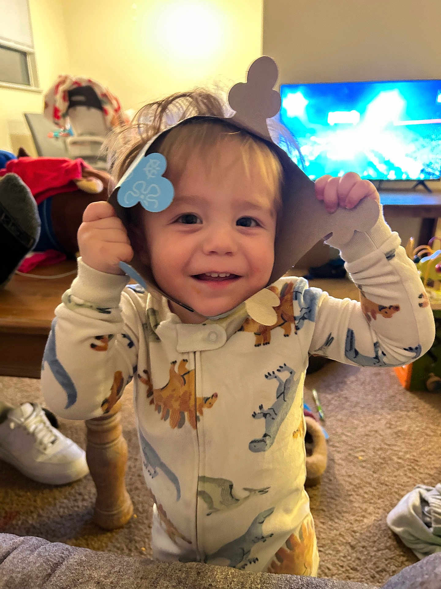 Benjamin joined the competition — help win amazing prizes! toddler, child, smiling, dinosaur_onesie, paper_crown, indoor, living_room, carpet, television, toy, furniture, happy, cute, playful, person, clothing, footwear, hair, home, cozy