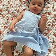 Léna a rejoint le concours — aidez-le/la à gagner de superbes lots ! baby, barefoot, blue_dress, bow, child, cute, floral_quilt, foot, hand, happy, headband, indoors, infant, lying_down, person, playful, portrait, skin, smile, toy