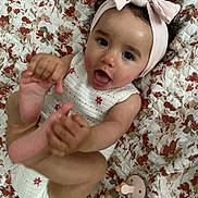 Léna a rejoint le concours — aidez-le/la à gagner de superbes lots ! baby, bow, child, closeup, clothing, cute, feet, floral_pattern, foot, hand, happy, headband, indoors, infant, lying_down, pacifier_clip, pink, playing, quilt, smiling