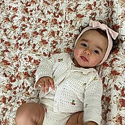 Léna participe au concours pour gagner de l'argent avec cette photo : baby, bedspread, bow, child, cozy, cute, face, floral_quilt, foot, hand, headband, indoors, infant, knitted_clothing, lying_down, pattern, person, playful, soft_texture, white_outfit