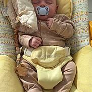 Mayron a rejoint le concours — aidez-le/la à gagner de superbes lots ! baby, sleeping, pacifier, plush_toy, baby_seat, yellow, onesie, soft_toy, infant, child, cute, comfort, indoor, peaceful, rest, fabric, cushion, wooden_toy, baby_accessory, relaxation