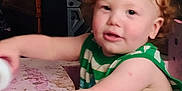 Timothy joined the competition — help win amazing prizes! toddler, child, curly_hair, red_hair, green_shirt, striped_clothing, indoor, playful, furniture, flowers, table, person, young_child, cute, smiling, skin, face, arm, expression, home