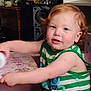 toddler, child, curly_hair, red_hair, green_shirt, striped_clothing, indoor, playful, furniture, flowers, table, person, young_child, cute, smiling, skin, face, arm, expression, home