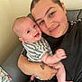 Logan is registered to the contest to win money with this photo: baby, adult, smiling, couch, striped_clothing, tattoo, indoor, person, holding, happy, face, arm, hand, casual_clothing, seated, closeup, infant, parent, toddler, home