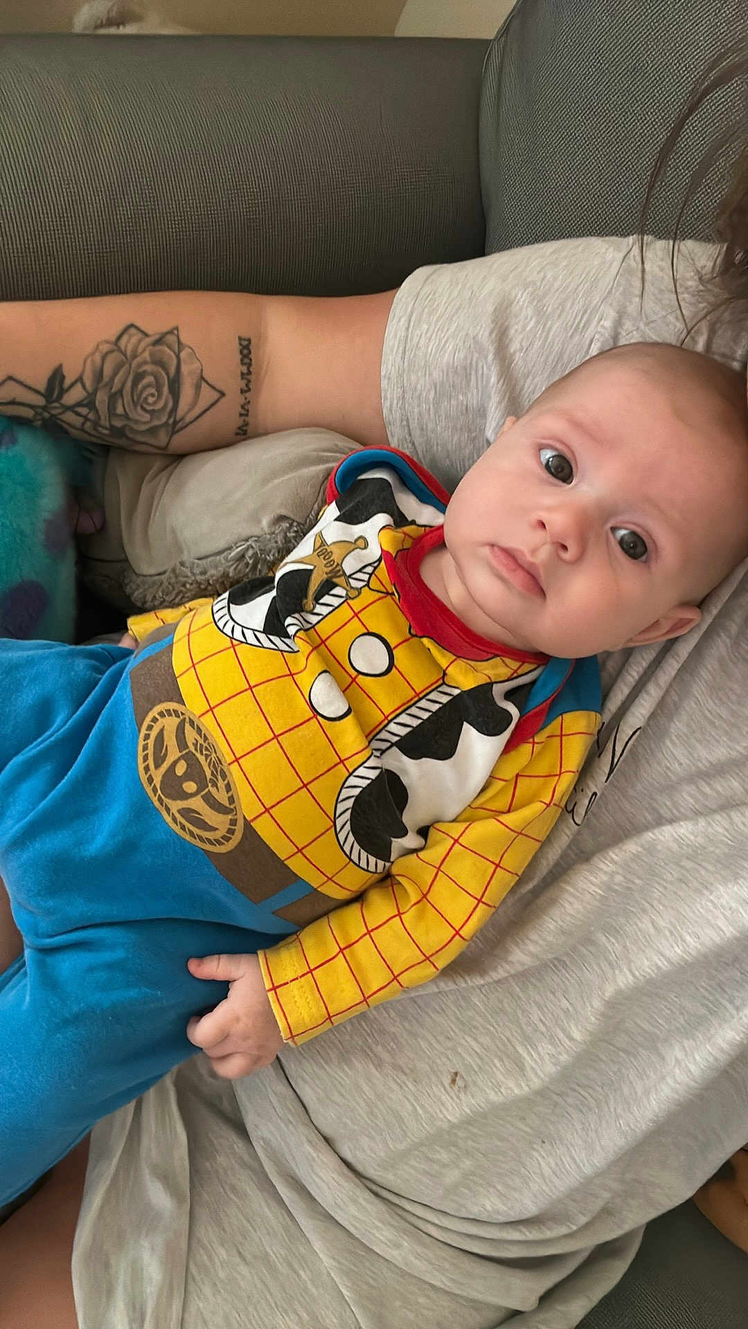 Logan is registered to the contest to win money with this photo: baby, child, person, tattoo, arm, clothing, cowboy_outfit, yellow_shirt, blue_pants, indoor, sofa, couch, casual, portrait, infant, cute, relaxing, human, face, expression