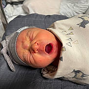 Grady is registered to the contest to win money with this photo: newborn, baby, infant, yawning, swaddled, blanket, hat, sleeping, face, mouth_open, headwear, bed, pillow, indoors, cozy, cute, resting, person, newborn_baby, soft