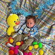 Oaklyn is registered to the contest to win money with this photo: baby, plush_toy, duck, stuffed_animal, easter_eggs, blanket, patterned, child, indoor, colorful, toy, clothing, cute, sitting, young_child, fabric, playful, soft_toys, portrait, infant