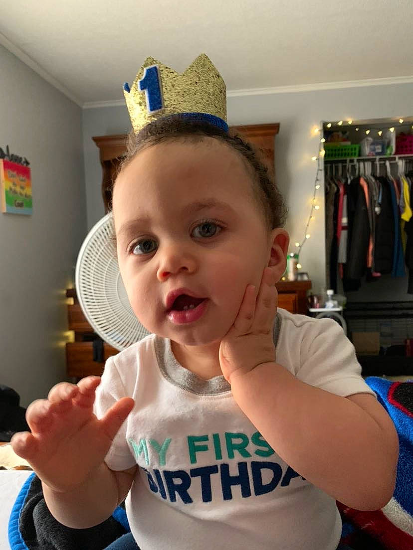 Kyndrick is registered to the contest to win money with this photo: arm, baby, baby_toddler_clothing, blue, cap, chair, costume_hat, facial_expression, finger, fun, gesture, hairstyle, hand, happy, party_supply, person, room, sleeve, t_shirt, thumb
