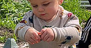 Jameson is registered to the contest to win money with this photo: toddler, child, outdoor, garden, plant, greenery, lantern, toy, curious, clothing, person, adult_hand, nature, sunlight, daytime, playing, exploring, casual_wear, footwear, expression