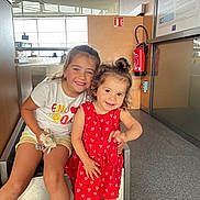 Margot participe au concours pour gagner de l'argent avec cette photo : child, children, girl, smile, happy, indoor, red_dress, white_shirt, toy, curly_hair, long_hair, modern_interior, floor, bench, window, fire_extinguisher, casual_clothing, playful, cute, portrait