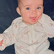 Bella is registered to the contest to win money with this photo: baby, infant, child, smiling, face, onesie, hand, blue_eyes, cute, happy, portrait, sitting, cozy, animal_print, soft_background, skin, expression, young, indoors, closeup