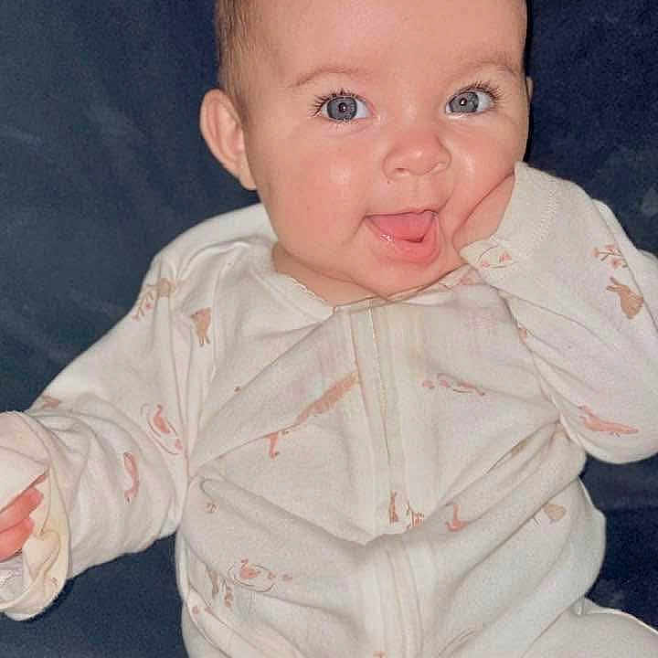 Bella is registered to the contest to win money with this photo: animal_print, baby, blue_eyes, child, closeup, cozy, cute, expression, face, hand, happy, indoors, infant, onesie, portrait, sitting, skin, smiling, soft_background, young