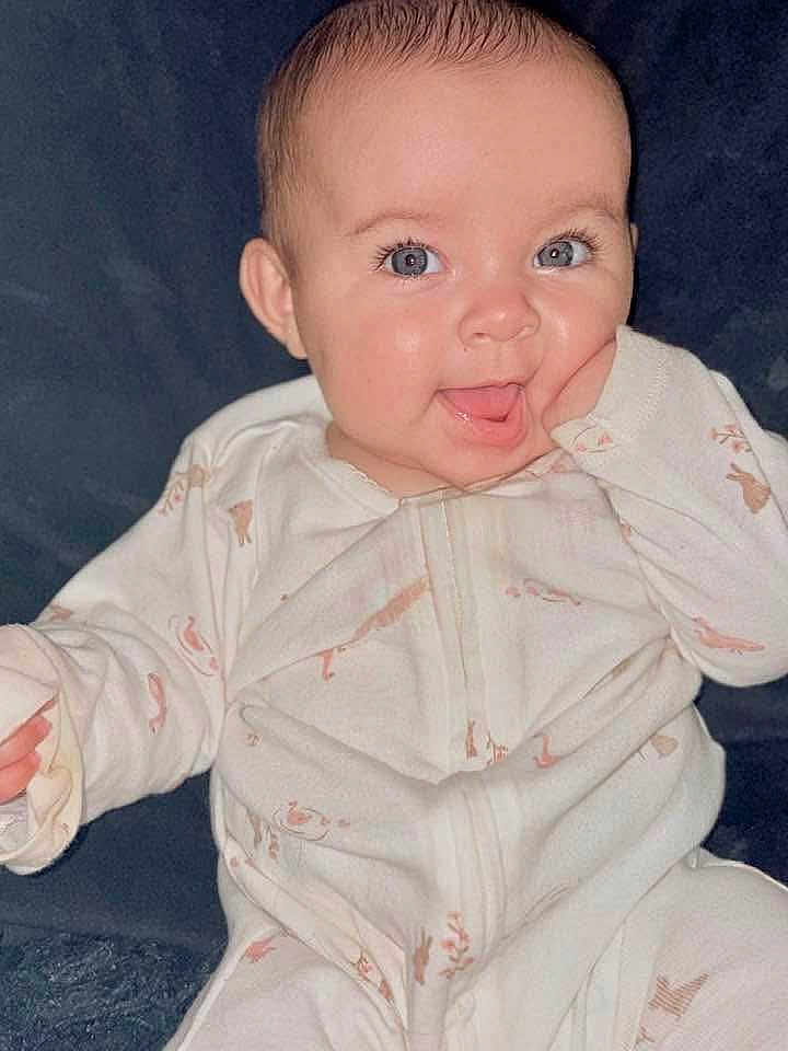 Bella is registered to the contest to win money with this photo: baby, infant, child, smiling, face, onesie, hand, blue_eyes, cute, happy, portrait, sitting, cozy, animal_print, soft_background, skin, expression, young, indoors, closeup