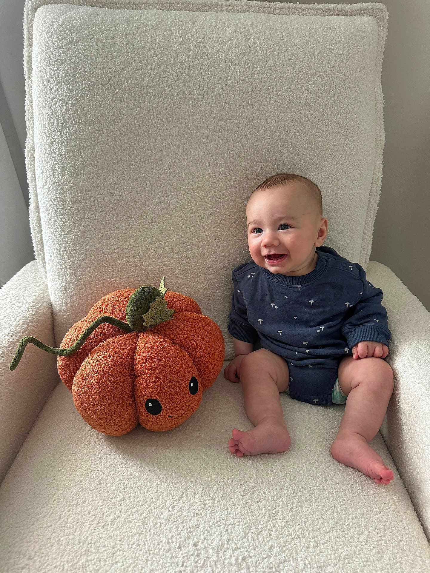 Colton is registered to the contest to win money with this photo: baby, child, plush_pumpkin, armchair, cozy, smiling, indoor, onesie, cute, soft_texture, orange, cream_color, happy, sitting, toy, infant, cushion, decor, comfort, face